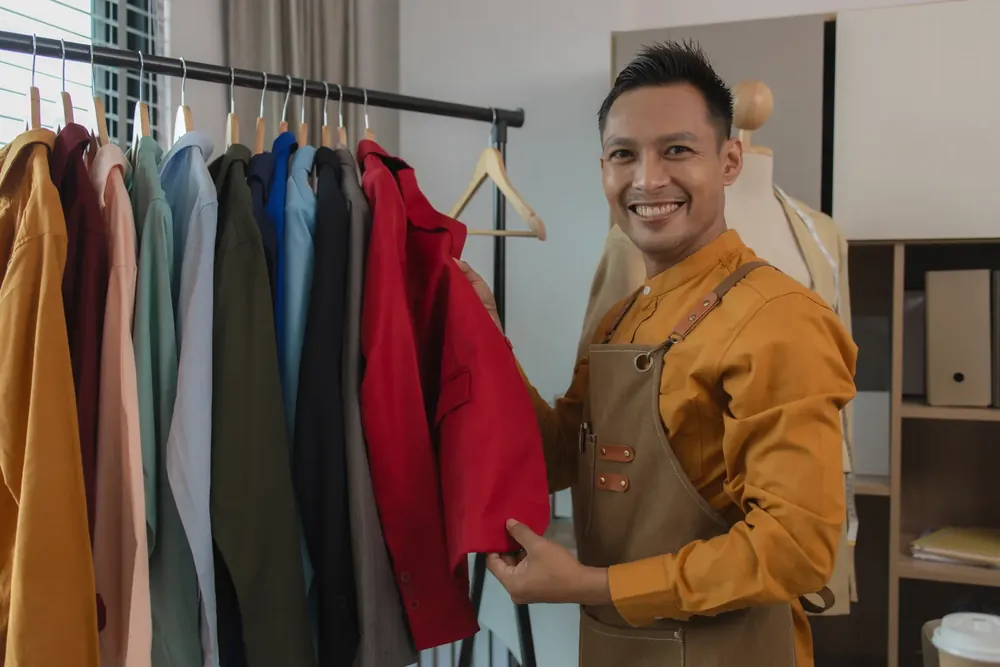 Pemilik kedai penjahit tersenyum semasa menunjukkan jaket