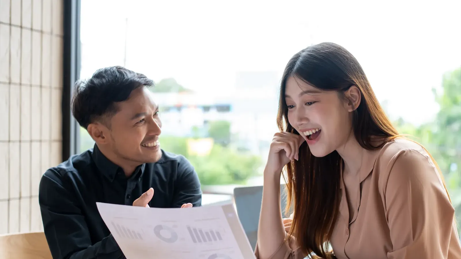 Two colleagues smiling over a printed report with charts